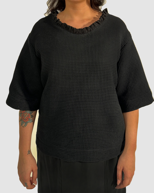 Vorderansicht eines schwarzen Shirts aus Waffelpique, mit gerüschtem Einsatz am Halsausschnitt aus Lyocell.